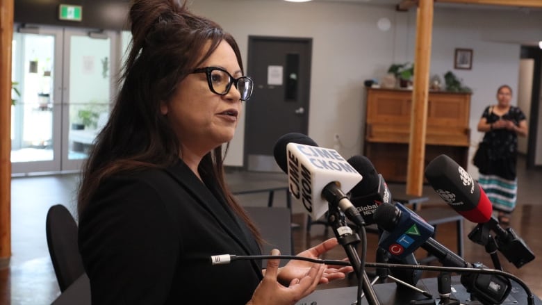 Woman wearing glasses stands in front of reporters' microphones