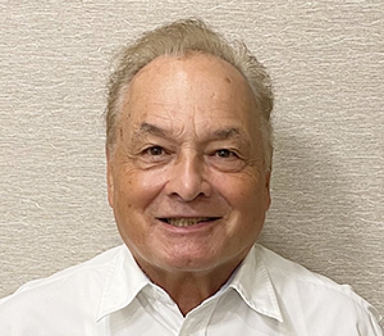 A man with white hair and shirt smiles.