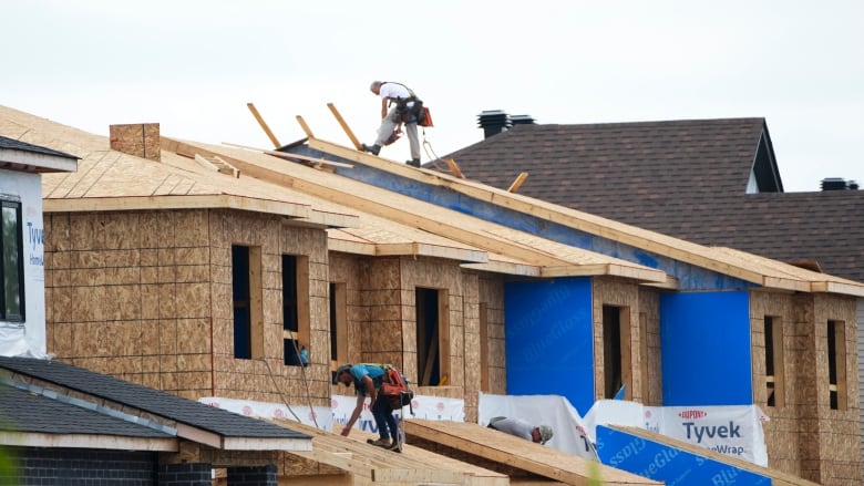 Two men work on the rooftops of houses under construction.