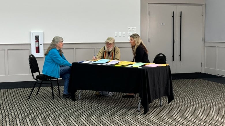 3 people sitting near a table talking to each other.