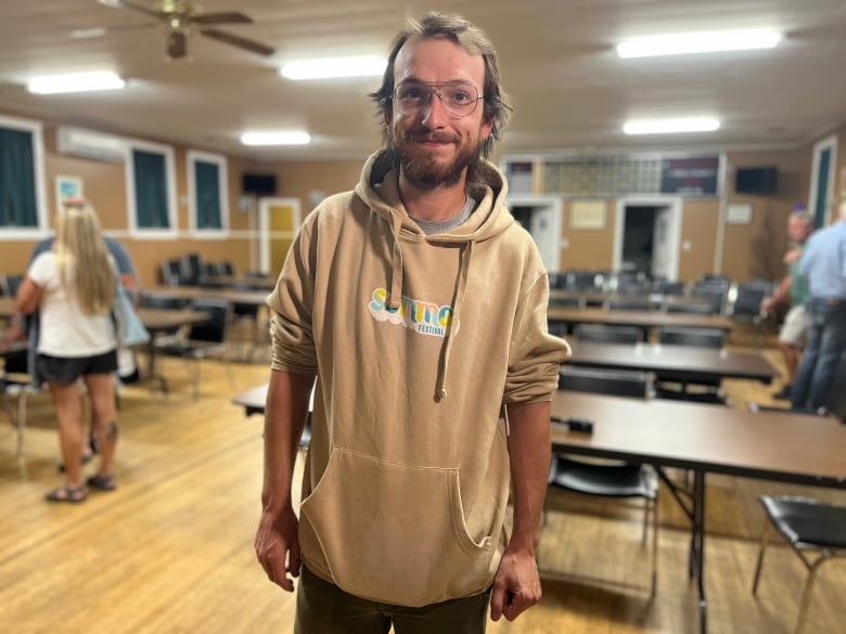 A young man with glasses poses for the camera in a nearly empty room. 