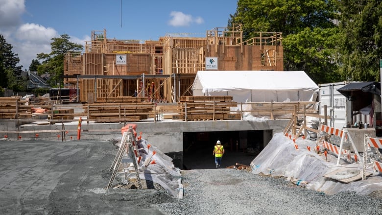 An under-construction home, with a worker in a high-vis vest entering an underground area.