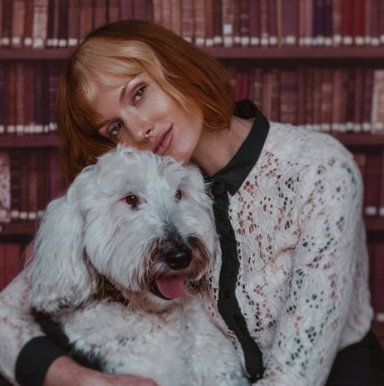 A woman holding a dog is sitting in front of a bookshelf. 