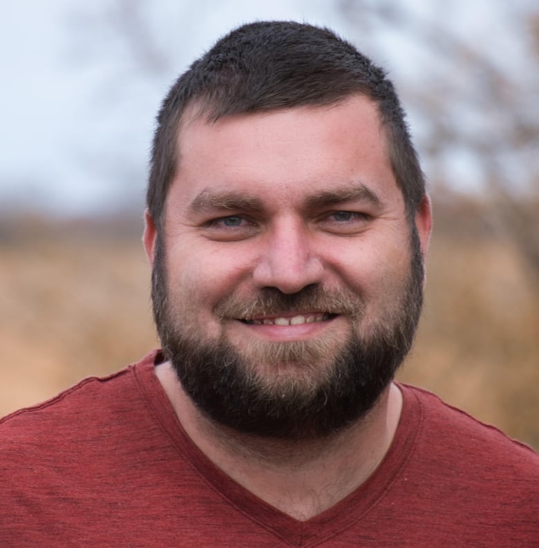 A headshot photo of a man with brown hair and brown beard smiling at the camera. 