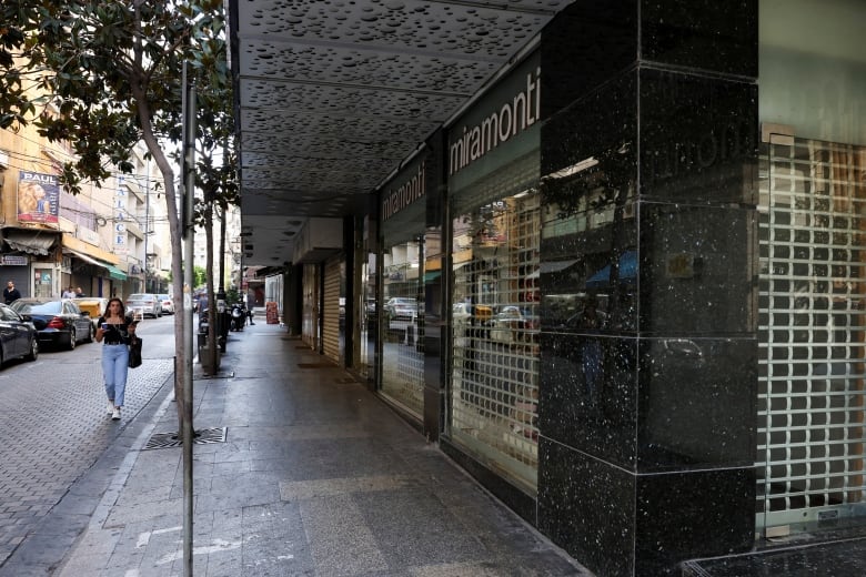 A woman in blue jeans walks along an urban street where the storefronts are all closed.