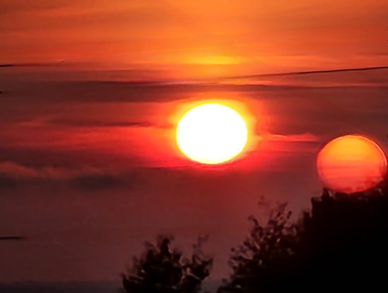 A rising sun turns the sky red and orange over a body of water.