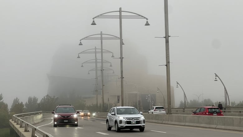 Cars are pictured with fog in the background obscuring a building.