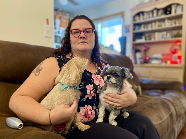 A woman sits on a couch, holding two small dogs.