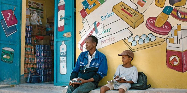 A man and a boy sit on a sidewalk.