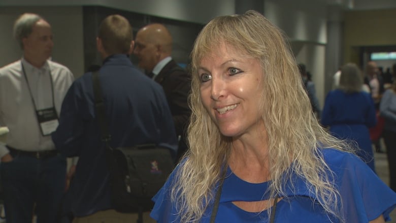 A woman with blond hair and a big smile speaks to a reporter.