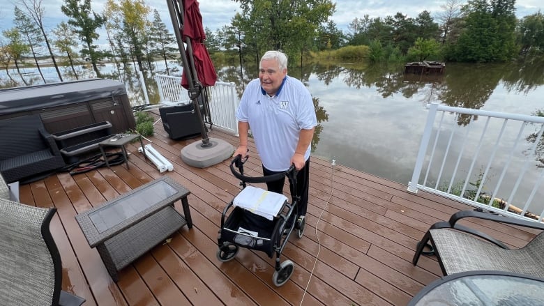 Man holding a mobility assisting device stands on a porch surrounded by water. 