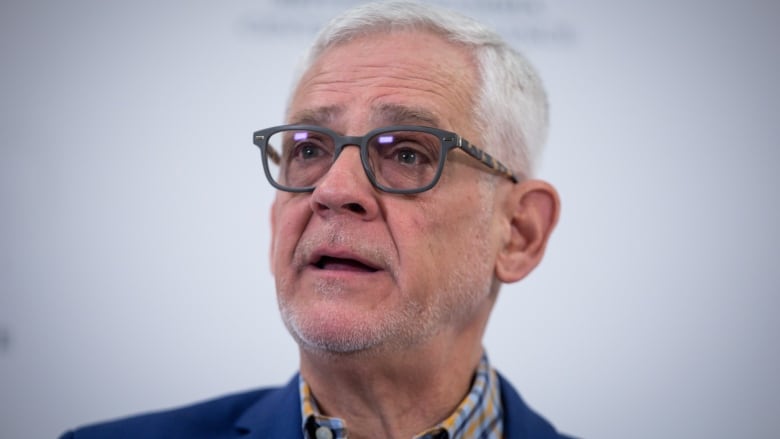 An older man with white hair wearing glasses speaks.