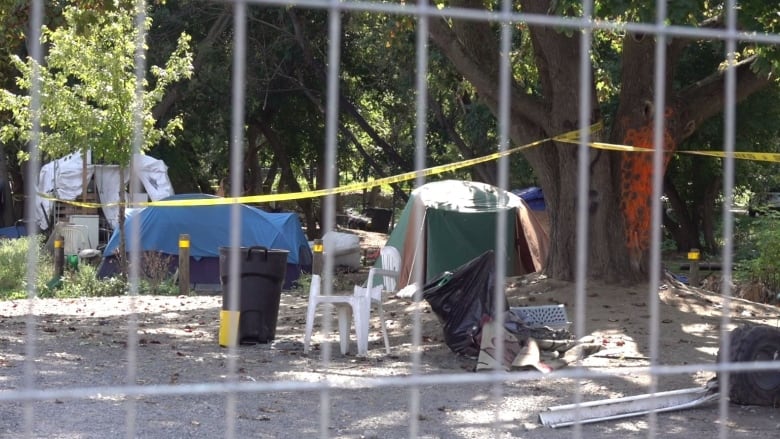 Tents hung with police tape can be seen through a fence. It's a sunny day.