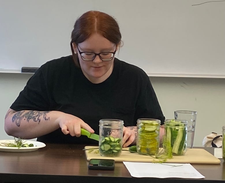 A woman chops vegetables on a cutting board that also holds jars filled with cut vegetables.