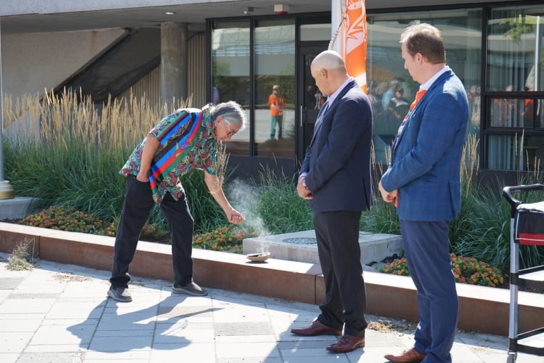 Greater Sudbury mayor Paul Lefebvre (right) stands besides Atikameksheng Anishnawbek Gimaa Craig Nootchtai (middle) as an elder smudges the survivor's flag.