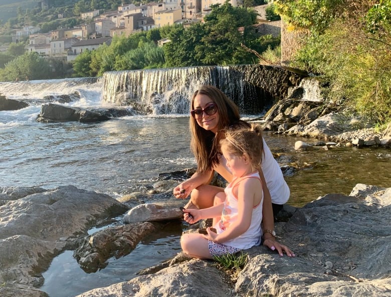 Mom and daughter sitting at rocky waterfront.