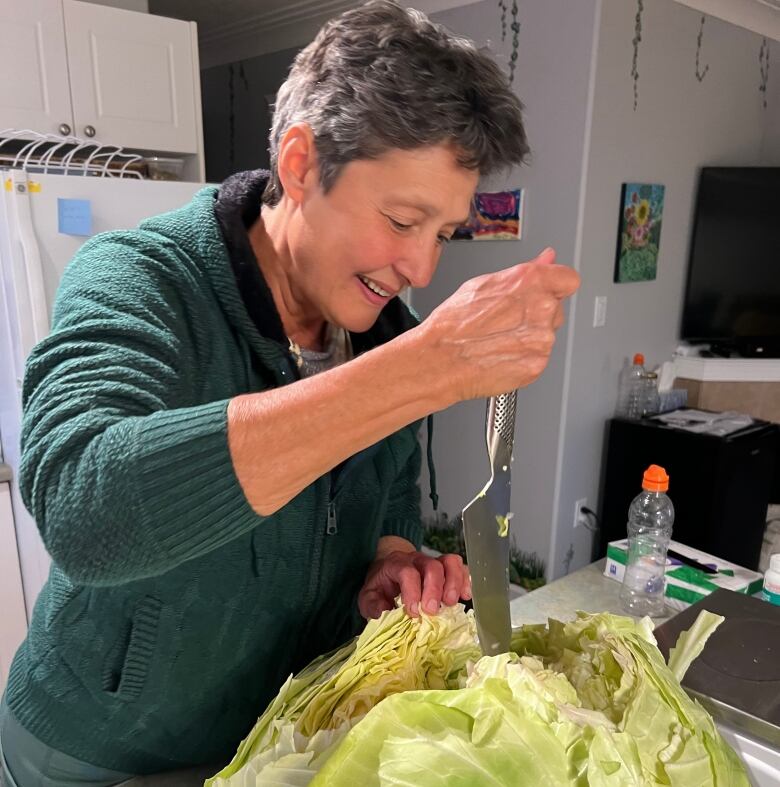 A woman cuts a knife into a very big green cabbage