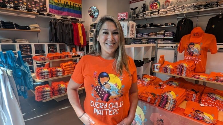 A woman wearing an orange shirt inside a store with several orange shirts and other apparel on display