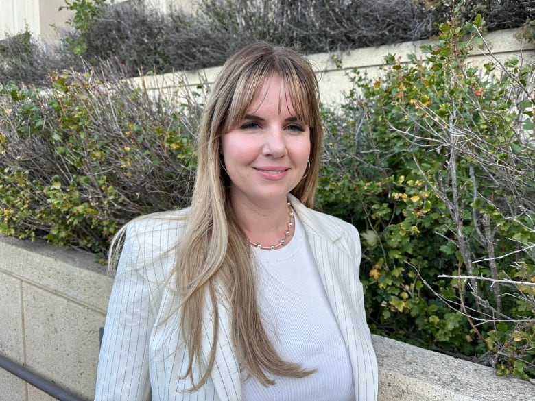 A woman with long hair stands in front of a building.