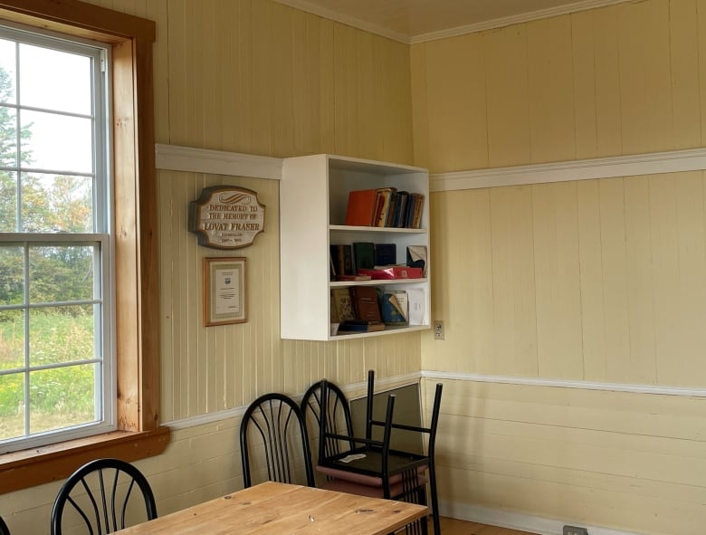 A room with yellow, wainscotted walls, table, chairs and a wood-framed window.