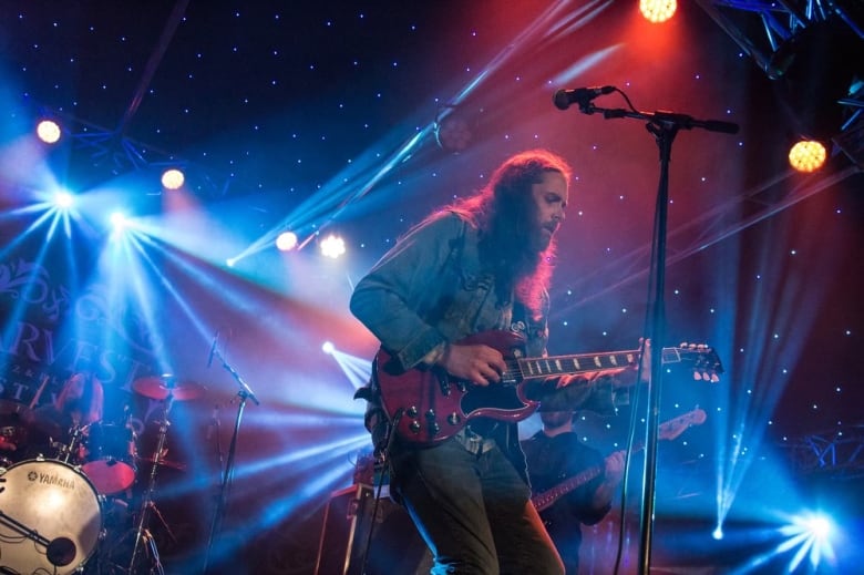 A man playing guitar on stage with red and blue lights around him