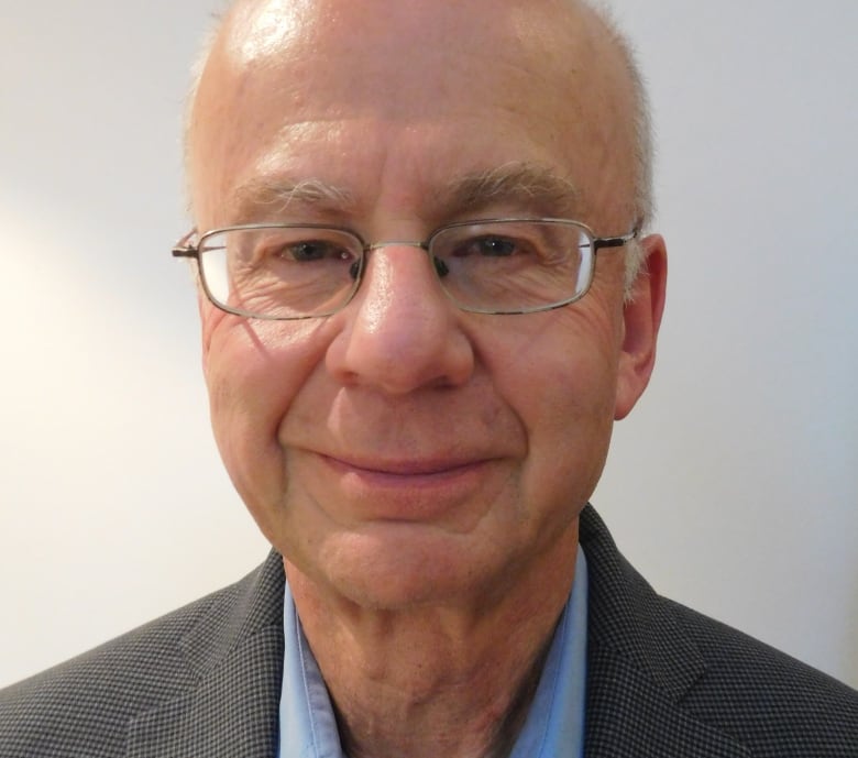 A man wearing glasses poses for a photo wearing a shirt and jacket.