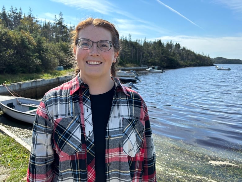 A woman with braided hair and glasses smiles at the camera while standing next to several recreational speed boats. 