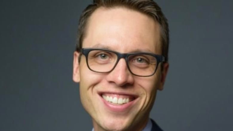 A man wearing glasses and a suit smiles in a head shot photo 