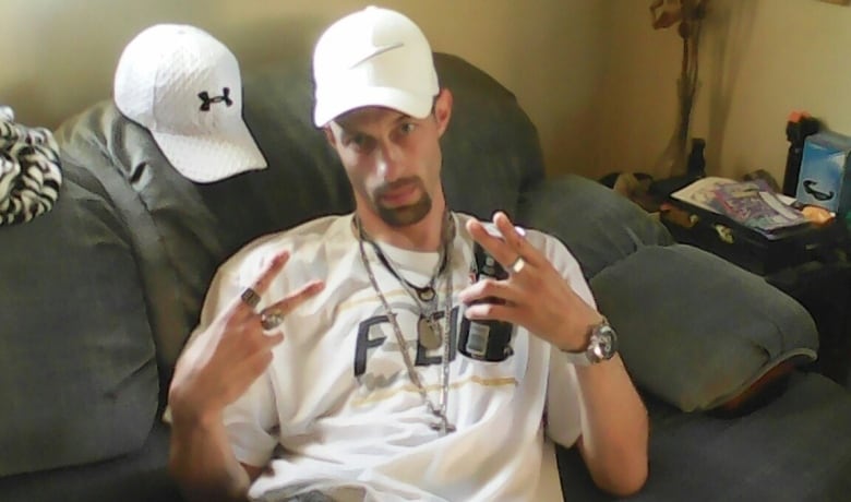 man in white had sitting back on a couch with both hands making a V sign with his fingers.