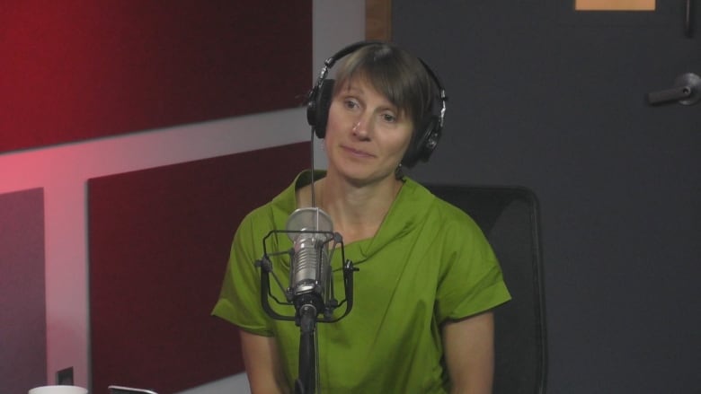 A woman wearing a green shirt sits in front of a microphone in a radio studio