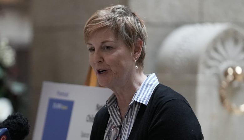 A woman speaks in front of microphones.