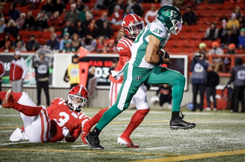 Kian Schaffer-Baker is running with the football tucked into his stomach area while calgary players try to tackle him