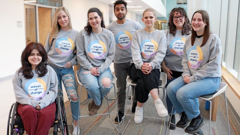 Seven people in grey sweaters that say Waves of Change. 