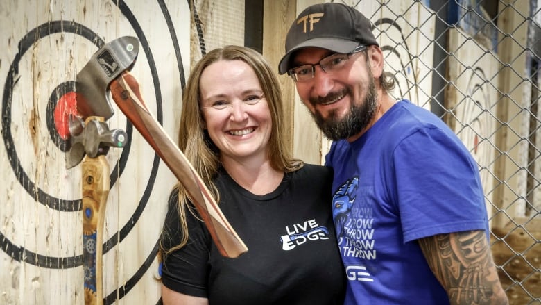 A woman and a man pose next to an axe-throwing target.