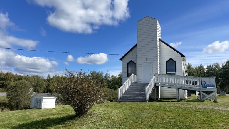 A small white church sits on a lawn of green grass. It's a sunny day and there's a blue sky above it. 