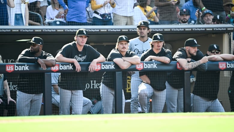 Male baseball players appear dejected while leaning over the railing of their team's dugout during a game.