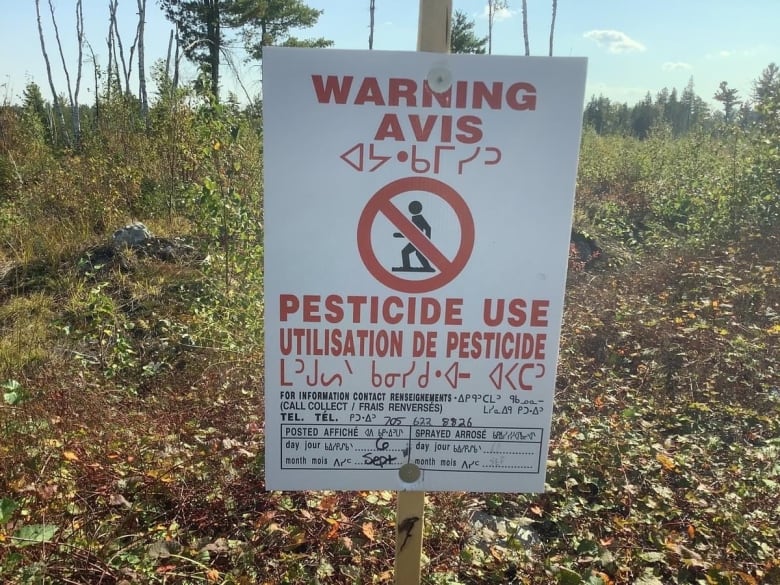 A sign that says pesticide use with a forest in the background.