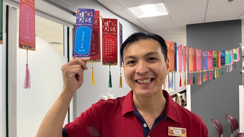 Man smiles while holding lantern banner with riddle on it.