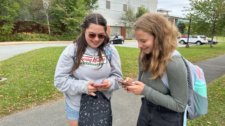 Two teenage girls are smiling as they look down at the cellphones outside a school in Halifax, N.S.