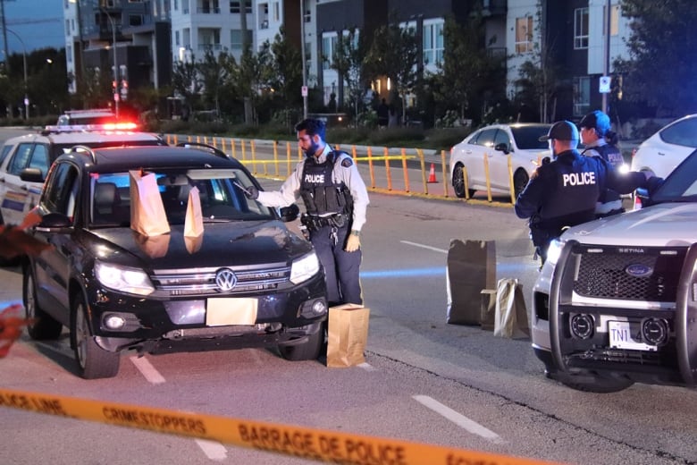 A shot-up car is seen with police nearby.