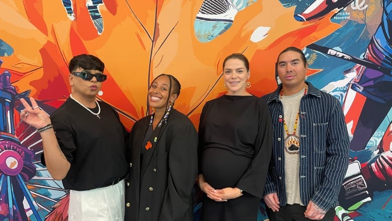 Four people pose for a group photo by a mural painting of Canadian icons. 