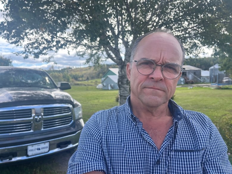 A man looks at the camera. Behind him is a truck 