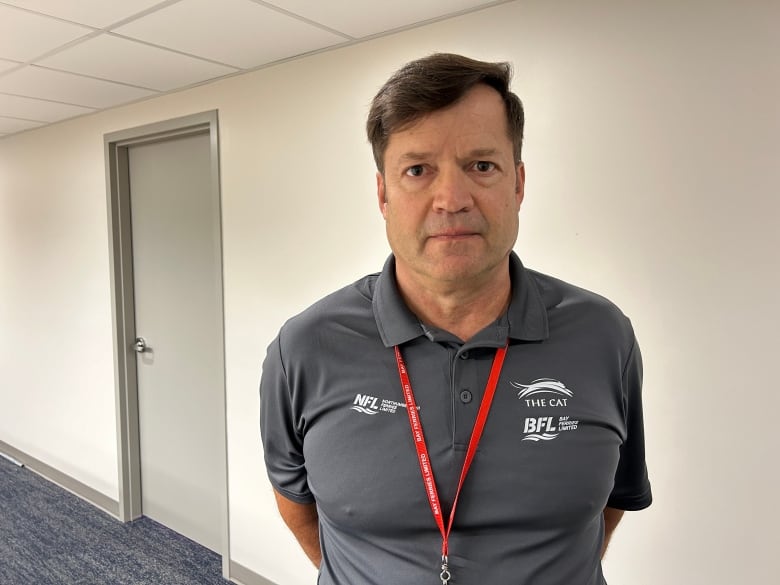 A man with short dark hair and a grey golf shirt with a Northumberland Ferries logo standing in a hallway.