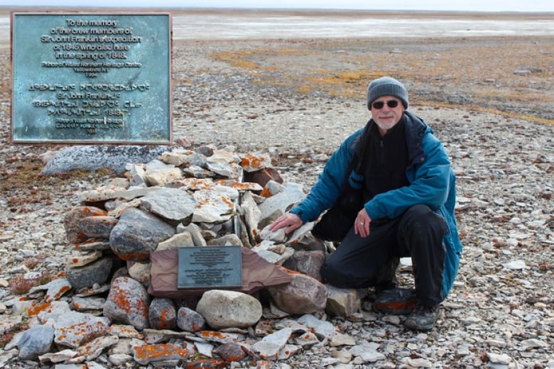 Douglas Stenton kneels beside where the remains of James Fitzjames and twelve other Franklin expedition sailors rest.