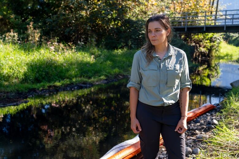 A woman wearing a grey shirt looks to her right next to a waterway on a sunny day.