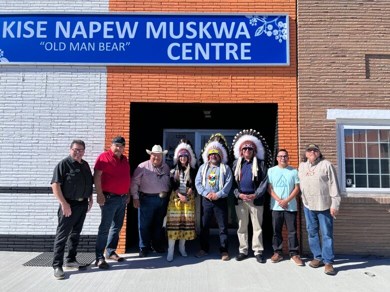 A group of people stand together under a sign on a building that reads 'Kise Napew Muskwa (old man bear) Centre