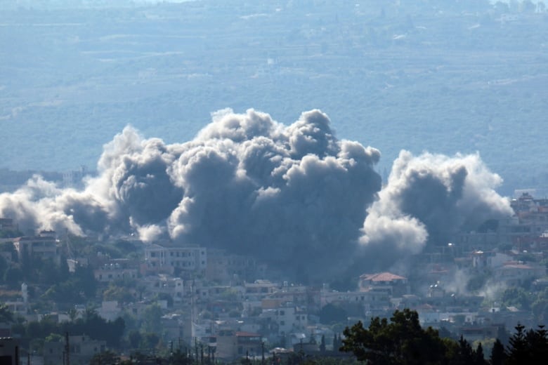 Huge clouds of smoke are shown above a town with low-rise buildings set in a valley.