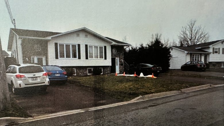 A residential street showing a duplex with tarps and orange cones on the driveway beside the righthand side of a duplex. 