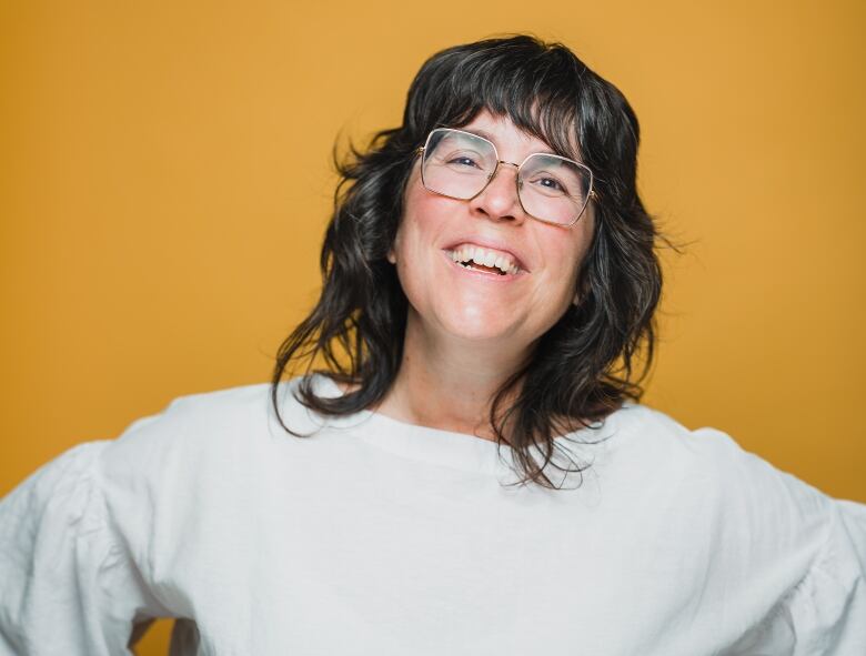 A smiling woman in front of a mustard yellow background