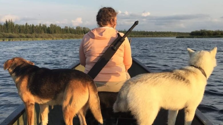 A woman on a canoe with two dogs behind her.